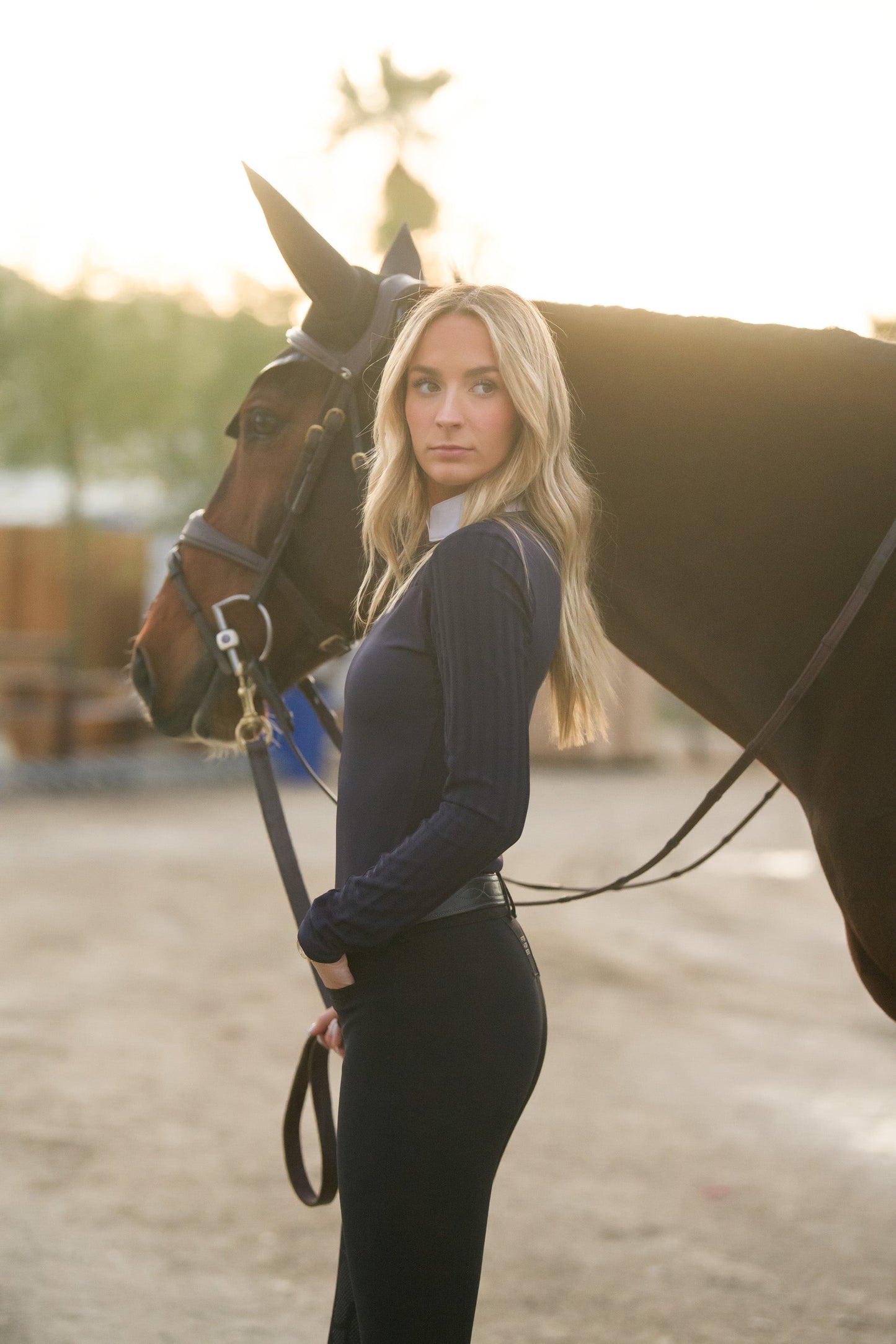 LOLLY Show Shirt navy by BellEq Equestrian Apparel, riding top worn beside horse at sunset on Tampa Home & Garden Store