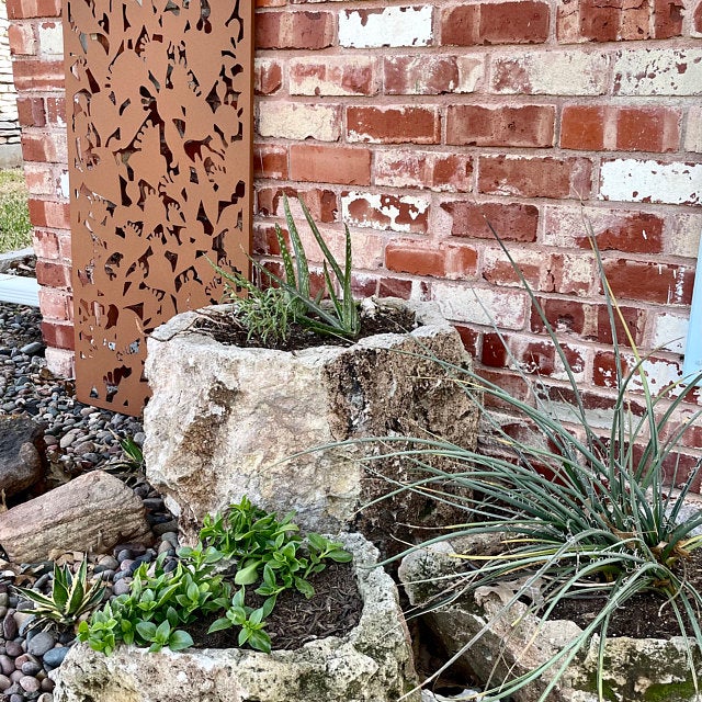 Outdoor metal privacy panel in heavy-duty steel, leaning by brick wall with planters on Tampa Home & Garden Store