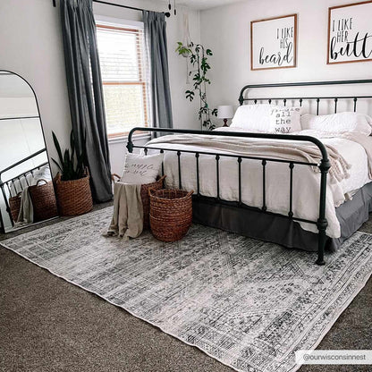 Barny Sage Flat Pile Washable Rug by Boutique Rugs under a black metal bed in a cozy bedroom on Tampa Home & Garden Store