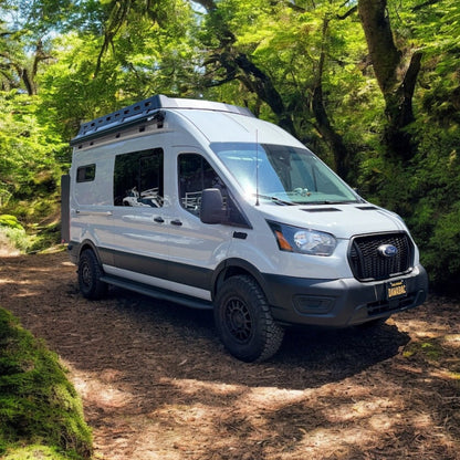 Avatar Ford Transit Rockbody Side Steps on white camper van with roof rack in a forest setting on Tampa Home & Garden Store