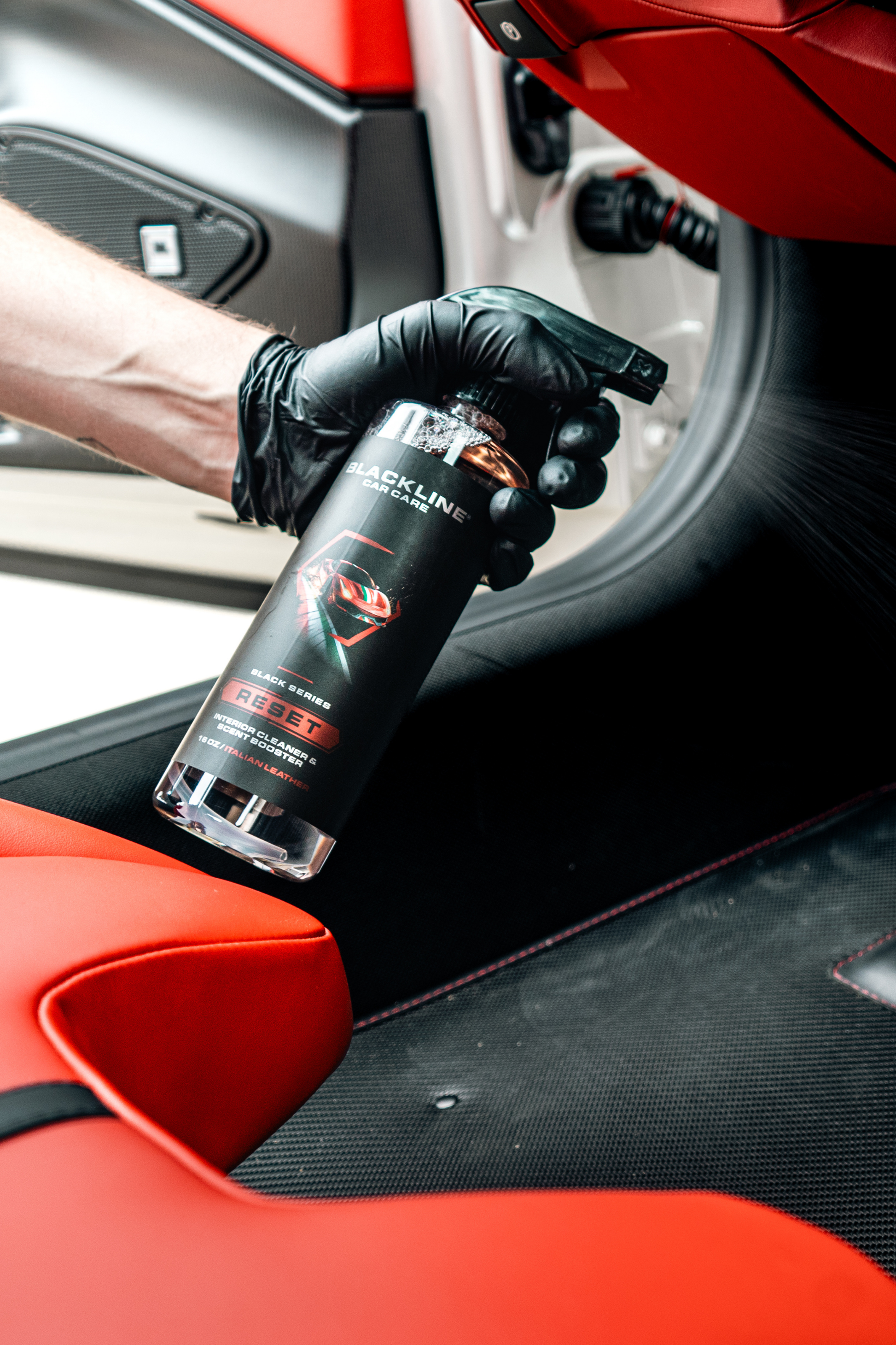 Blackline RESET Interior Cleaner & Scent Booster bottle held by gloved hand in red car on Tampa Home & Garden Store