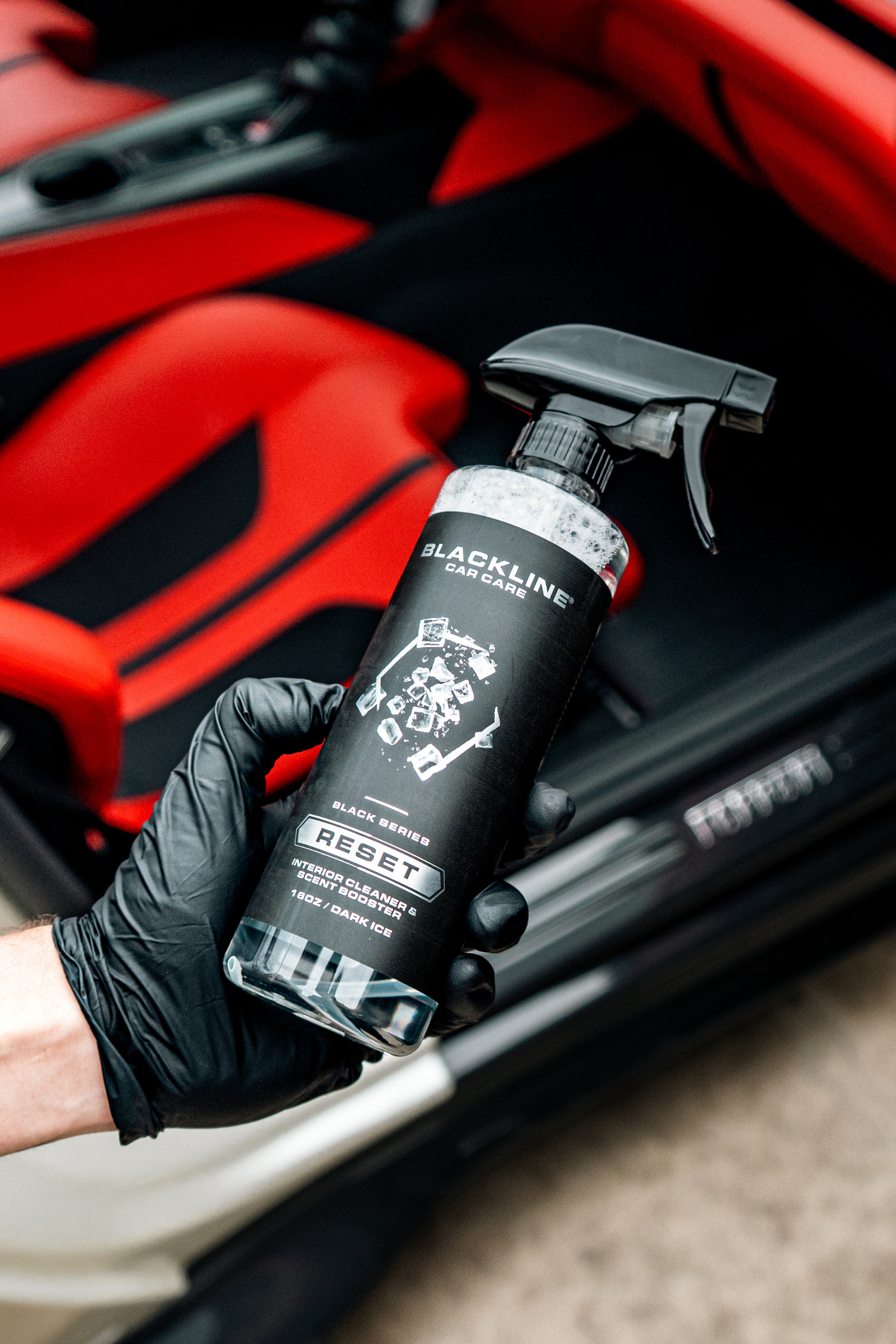Blackline RESET interior cleaner spray bottle held by gloved hand in red car interior on Tampa Home & Garden Store