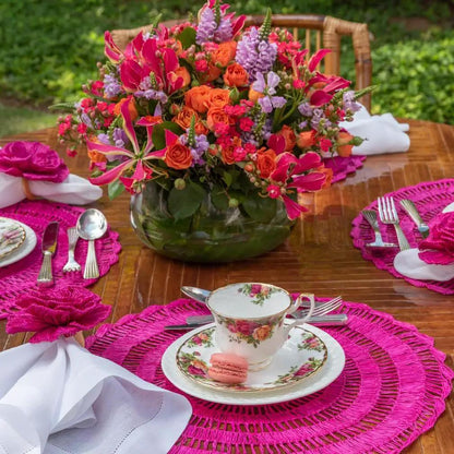 Buriti straw placemats by Talah Home in pink on wooden outdoor table with floral teacup setting on Tampa Home & Garden Store