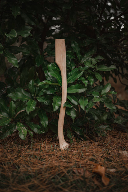 Whiskey River 28in axe handle in natural wood finish, standing upright among green leaves on Tampa Home & Garden Store
