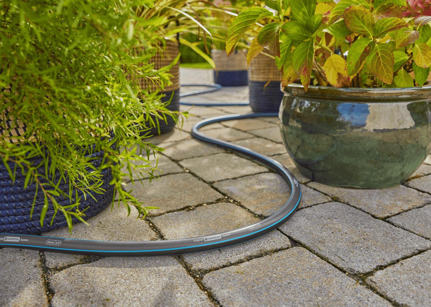 Gardena garden hose 30m 100ft 5/8 X-Flow coiled on stone patio beside potted plants on Tampa Home & Garden Store