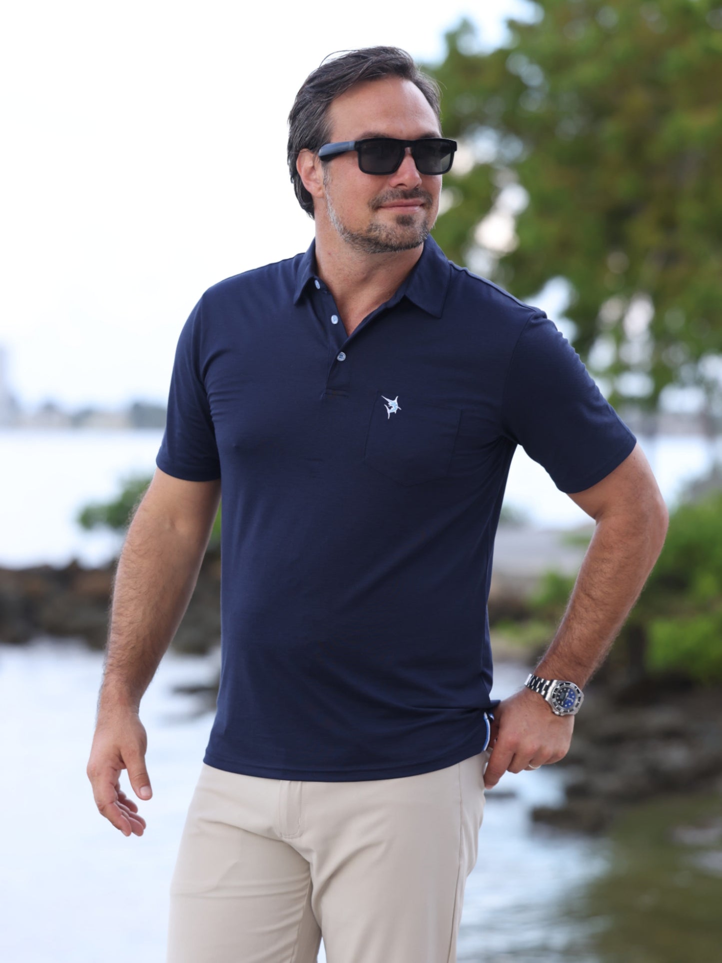 Charleston Polo navy polo shirt by White Water Life with chest logo, worn by man outdoors on Tampa Home & Garden Store
