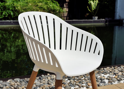 Nassau white armchair with wood legs, curved back and vertical slats by a pond outdoor dining on Tampa Home & Garden Store