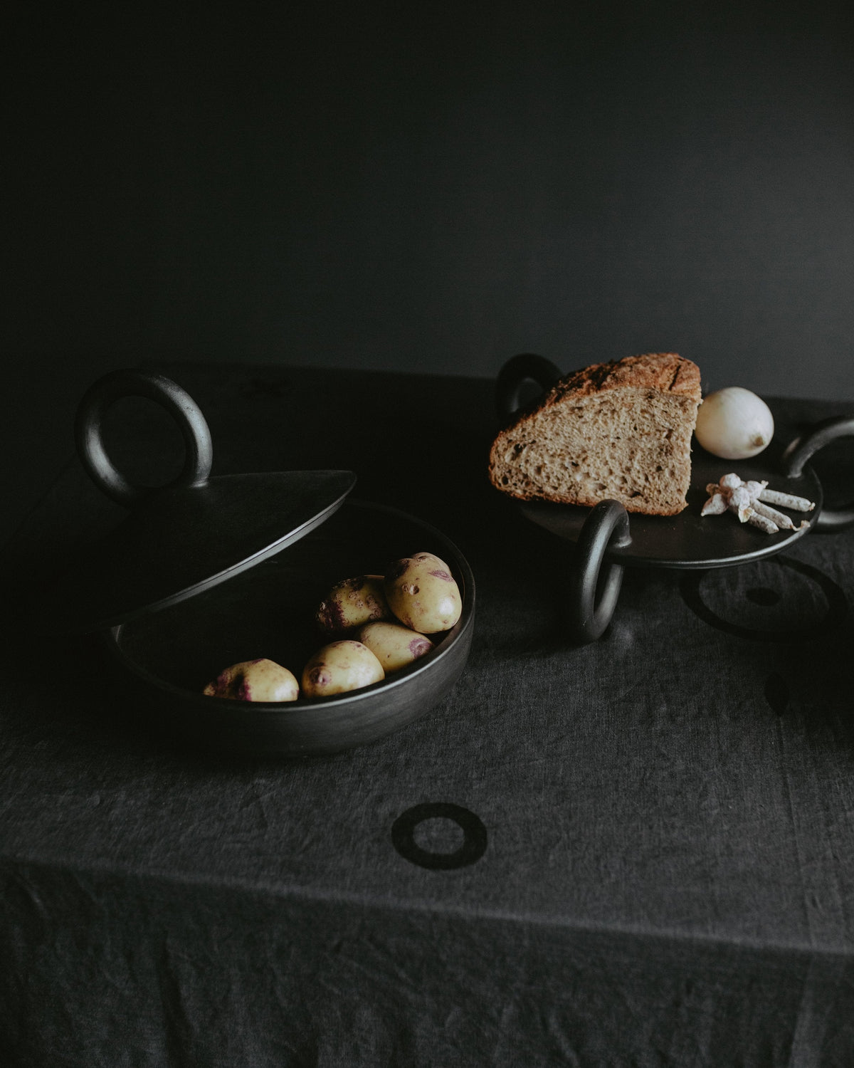 Large black serving platter with loaf of bread and several potatoes on a dark table on Tampa Home & Garden Store