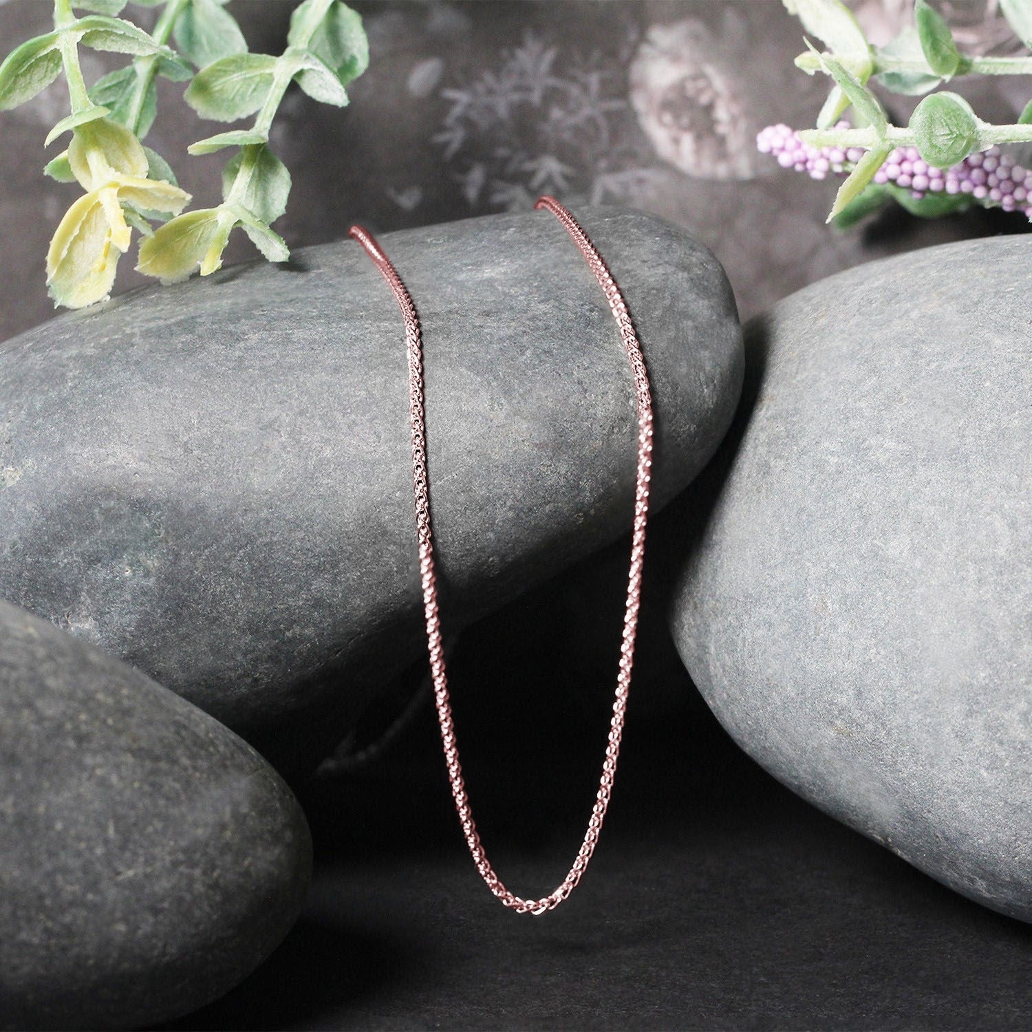 14k rose gold diamond-cut round wheat chain necklace 1.1mm, draped over smooth gray stones on Tampa Home & Garden Store