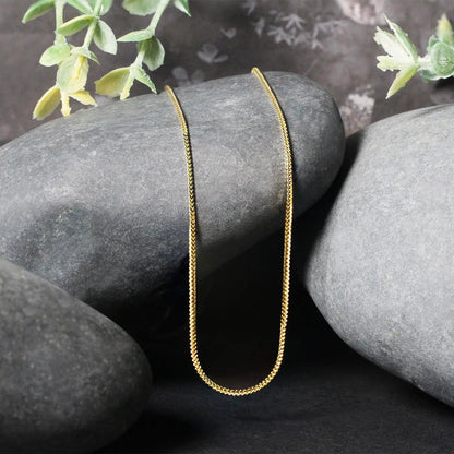 14k yellow gold Franco chain necklace 0.9mm, two slim chains draped over gray stones on Tampa Home & Garden Store