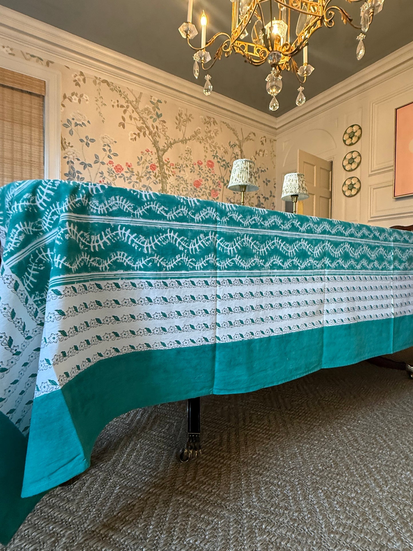 Bluebell Tablecloth in Emerald, teal border with white leaf pattern draped over a table on Tampa Home & Garden Store