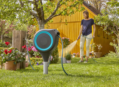 Gardena RollUp S 15m hose reel box with teal trim on stand; gardener waters with blue hose on Tampa Home & Garden Store