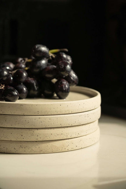 Stack of three handmade stoneware plates white with speckles topped by dark grapes on Tampa Home & Garden Store