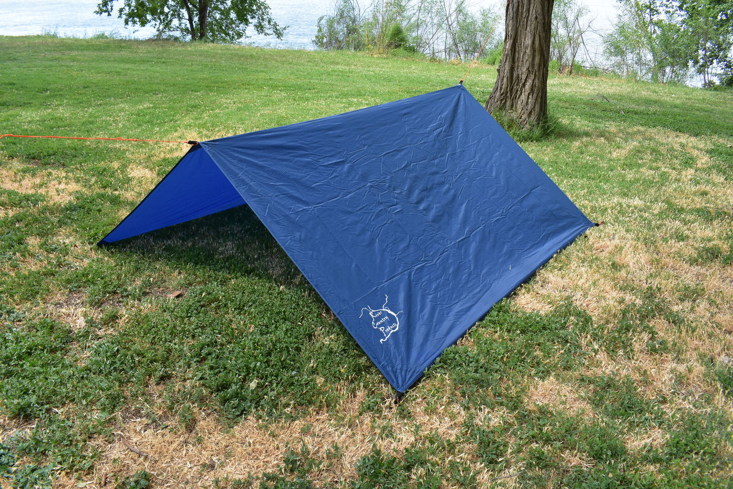Hammock Rain Fly tarp by River Country Gear, blue tarp with visible logo, pitched as shelter in park on Tampa Home & Garden Store
