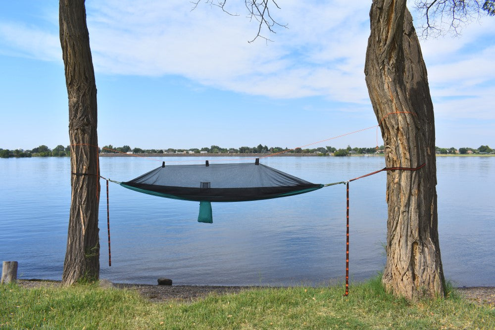 River Country Gear Hammock Tent black with teal edge hung between two trees over a calm lake on Tampa Home & Garden Store