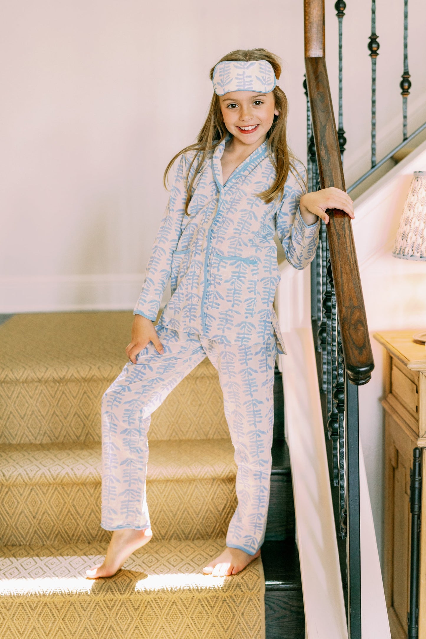 Mini Trellis Pajama Set in blue with leaf print, kid model on staircase wearing sleep mask on Tampa Home & Garden Store
