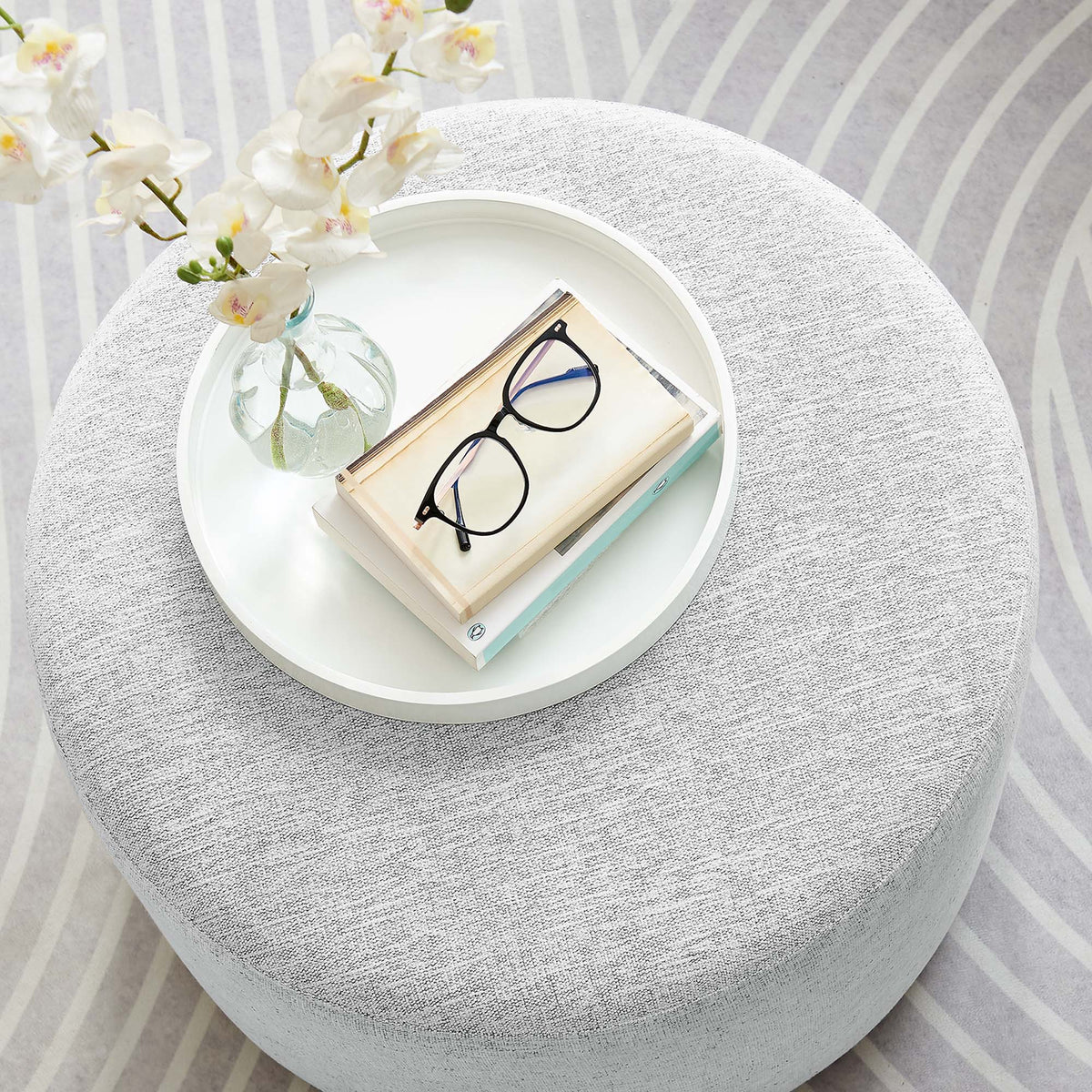 Callum round woven heathered gray fabric upholstered ottoman with white tray, vase and glasses on Tampa Home & Garden Store