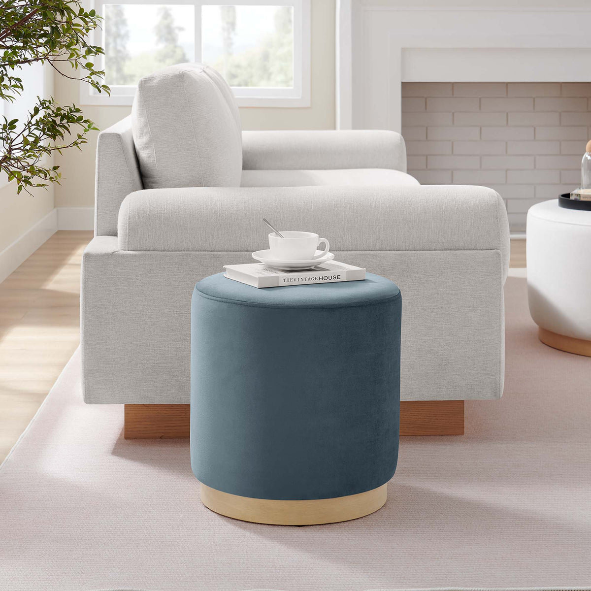 Tilden 16-inch round performance velvet ottoman in blue with gold base in a bright living room on Tampa Home & Garden Store