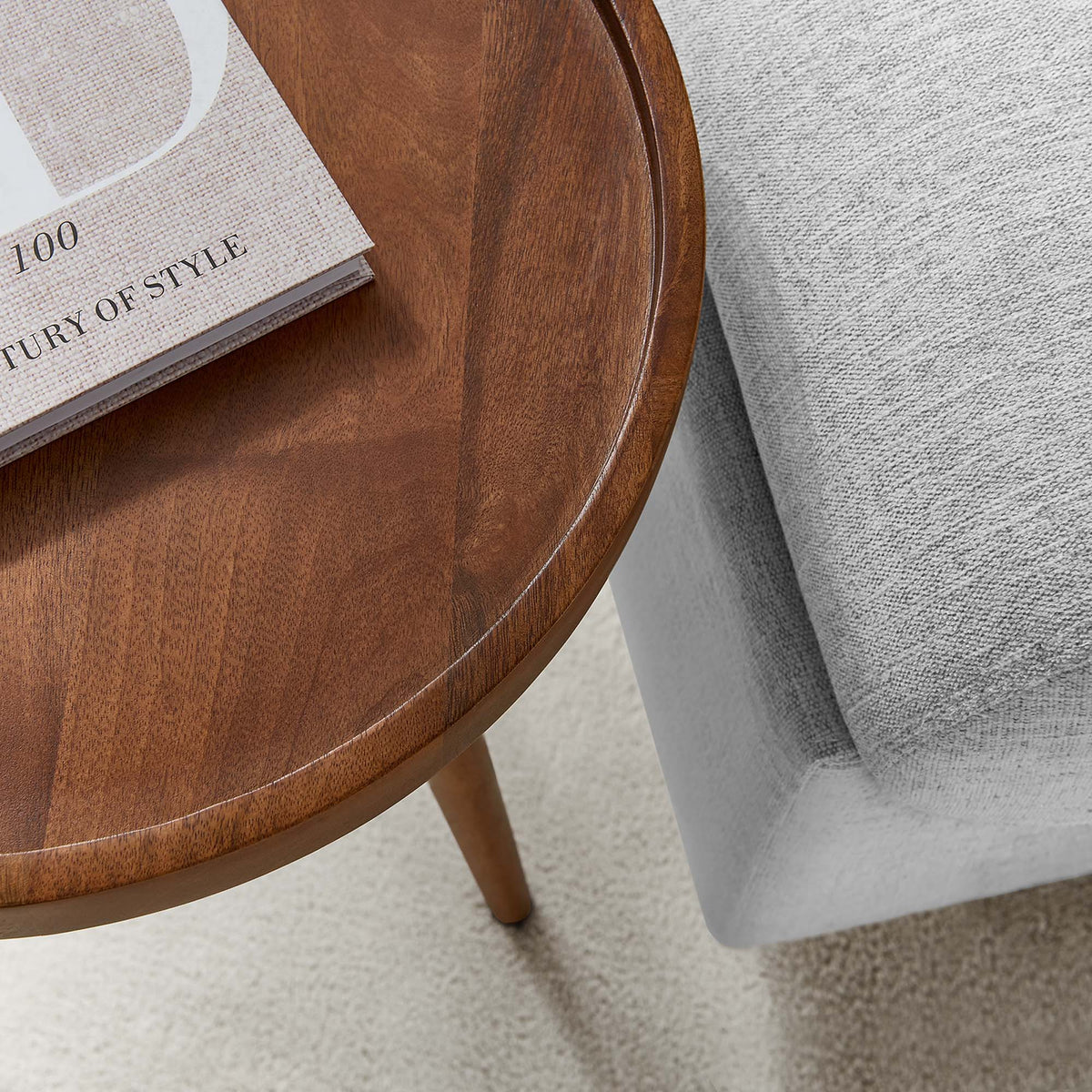 Chiro Round Wood Side Table warm brown finish with curved edge beside a grey sofa on Tampa Home & Garden Store