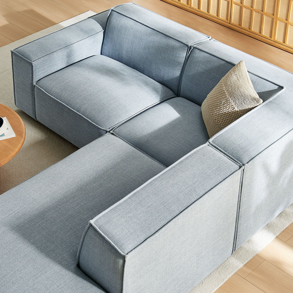 Modular L-shaped sectional sofa in light blue denim fabric with beige pillow on wood floor on Tampa Home & Garden Store