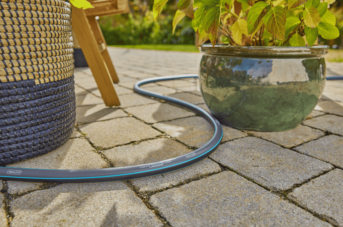 Gardena 30m/100ft garden hose 5/8 X-Flow coil on stone patio beside wicker furniture on Tampa Home & Garden Store