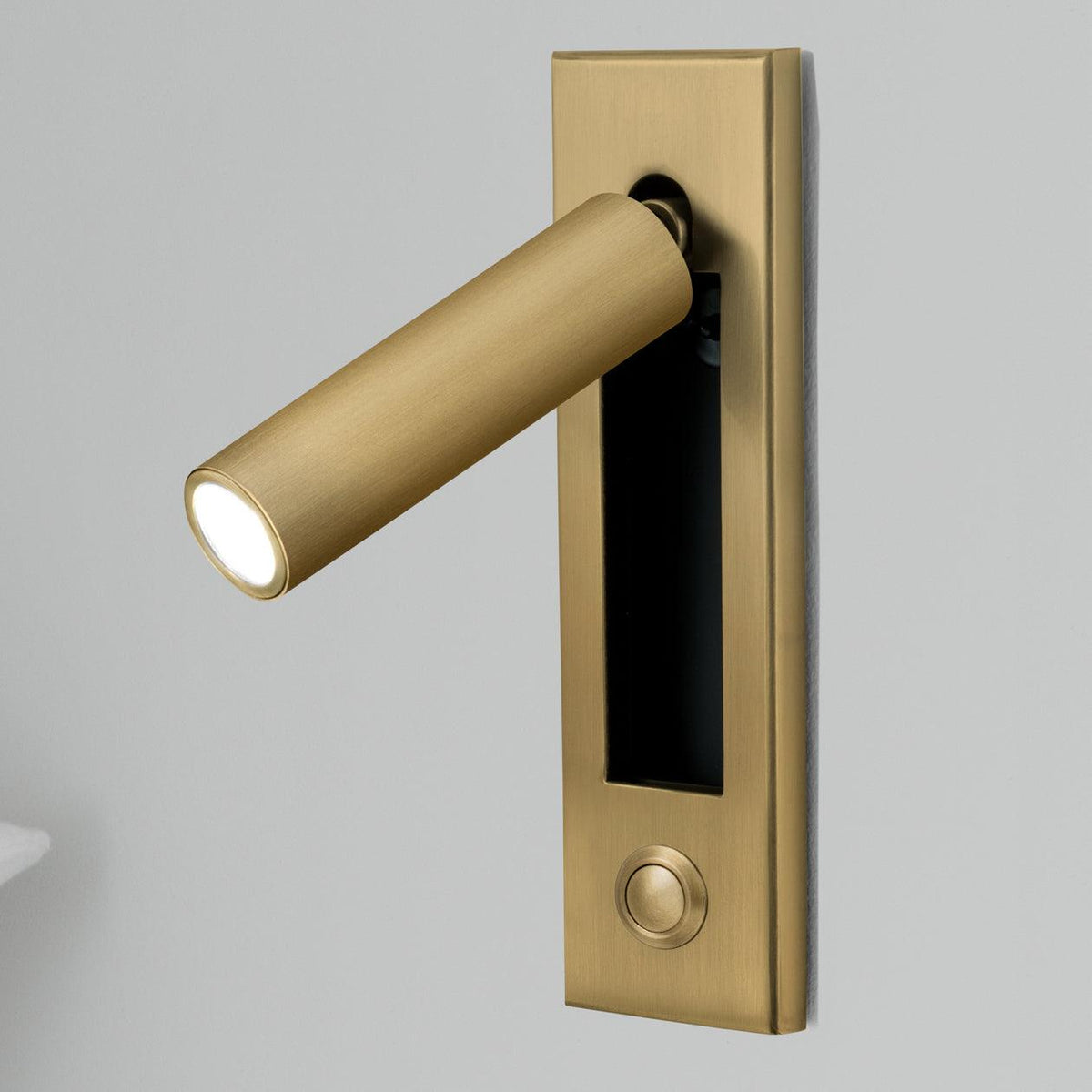Bedside wall sconce in brass with cylindrical warm LED light on a rectangular backplate on Tampa Home & Garden Store