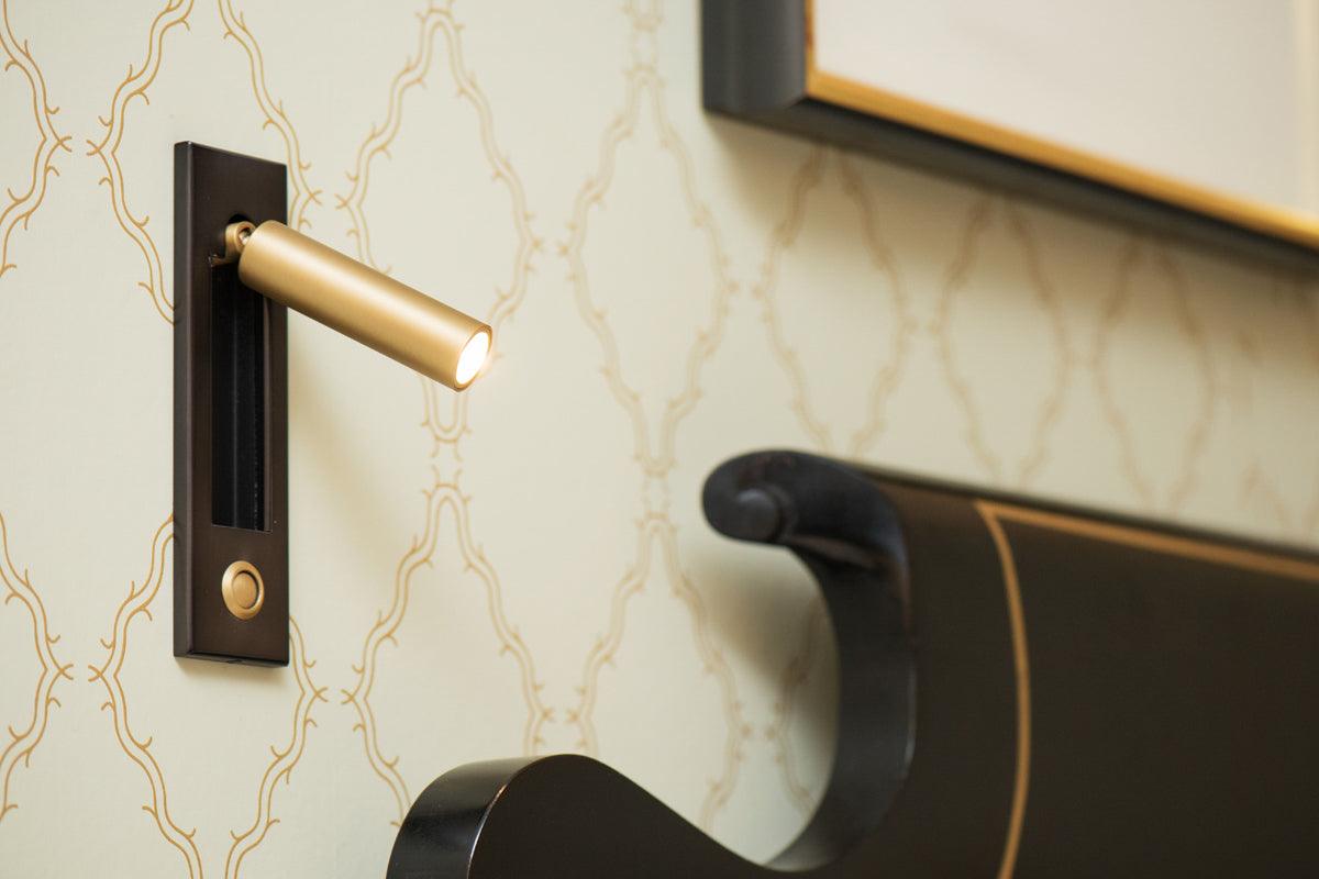 Moktan Sabai folding bedside wall sconce with gold LED cylinder on black mount, warm light on Tampa Home & Garden Store