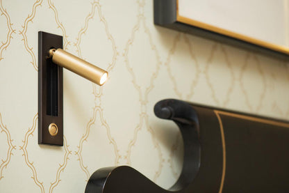 Moktan Sabai folding bedside wall sconce with gold LED cylinder on black mount, warm light on Tampa Home & Garden Store