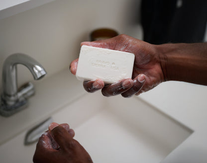 Bravo Sierra face & body cleansing bar, white bar soap in hands lathering under a faucet on Tampa Home & Garden Store