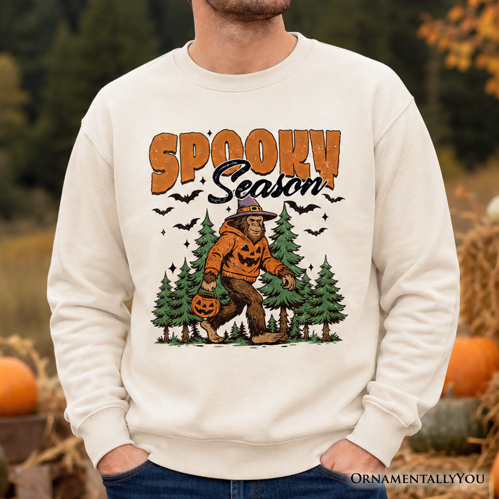 Spooky Season Bigfoot Sweatshirt with pumpkin Sasquatch in pines on beige fabric OrnamentallyYou on Tampa Home & Garden Store