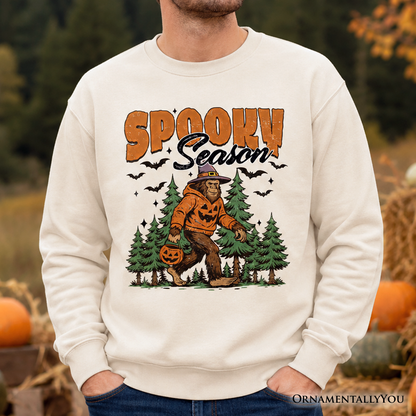 Spooky Season Bigfoot Sweatshirt with pumpkin Sasquatch in pines on beige fabric OrnamentallyYou on Tampa Home & Garden Store
