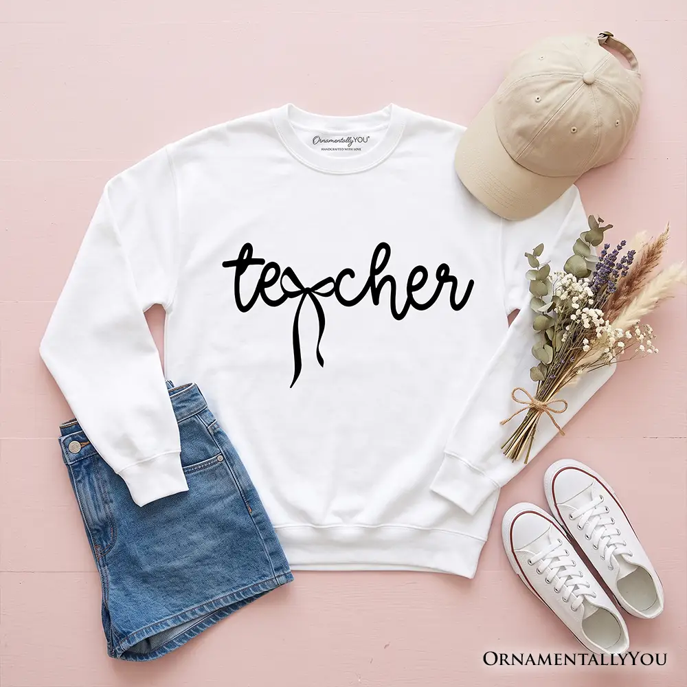 Teacher Coquette Bow Sweatshirt in white with black script, flatlay with denim shorts on Tampa Home & Garden Store