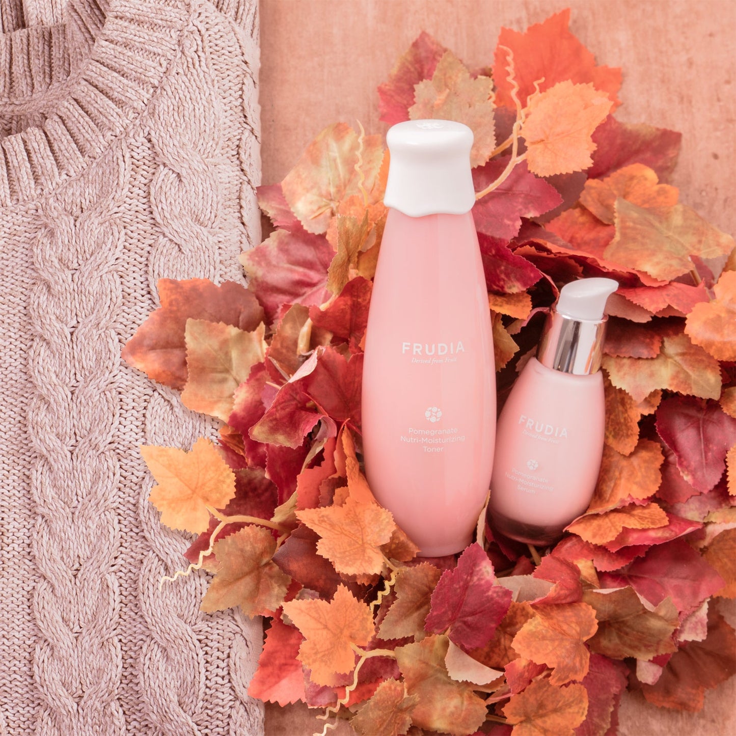 Frudia Pomegranate Nutri-Moisturizing Serum bottles in pink with white caps among autumn leaves on Tampa Home & Garden Store