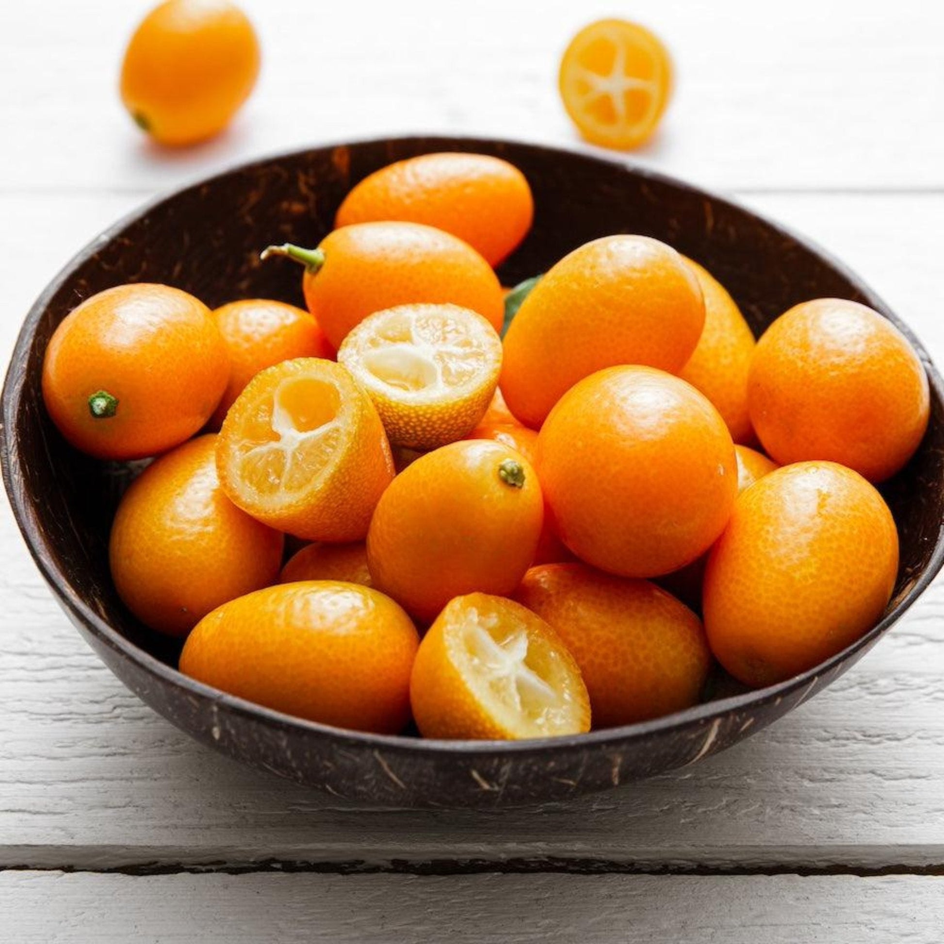 Fukushu kumquat fruits in a dark bowl; bright orange citrus, some halves show juicy segments on Tampa Home & Garden Store