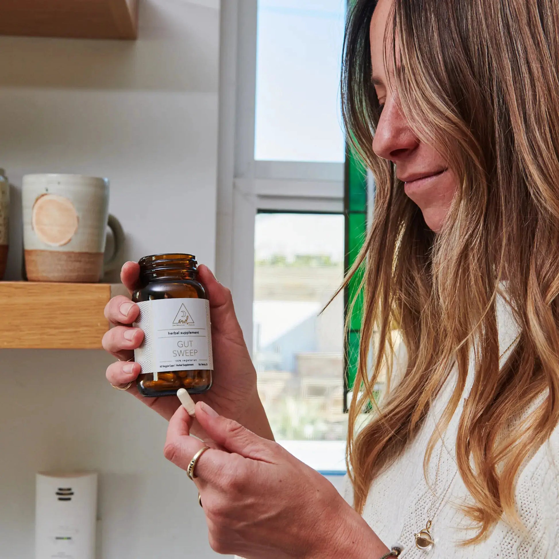 1-Week Gut Sweep Reset herbal supplement bottle by OWL Venice held by a woman in a kitchen on Tampa Home & Garden Store