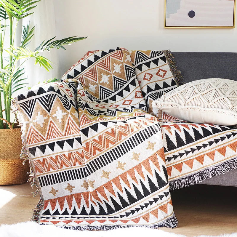 DecorBites Knitted Nordic Plaid Blanket draped over sofa in warm orange black cream tones on Tampa Home & Garden Store