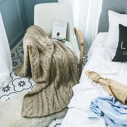 DecorBites Khaki Beige Chunky Knit Wool Blanket draped over a white chair in a bedroom on Tampa Home & Garden Store