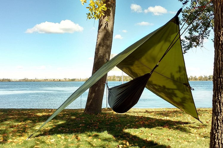 Hammock Rain Fly tarp in green over a black hammock between trees by a lakeside on Tampa Home & Garden Store