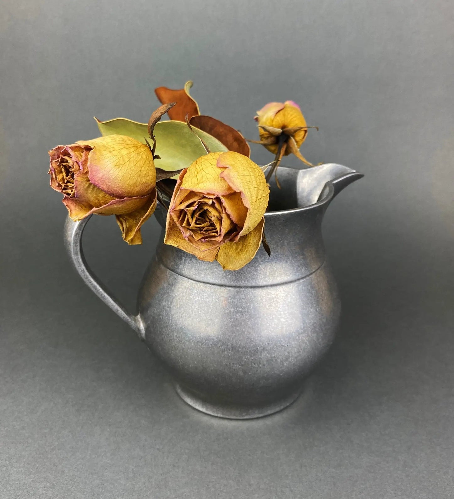 Metal pitcher vase with dried yellow roses centerpiece against gray backdrop on Tampa Home & Garden Store