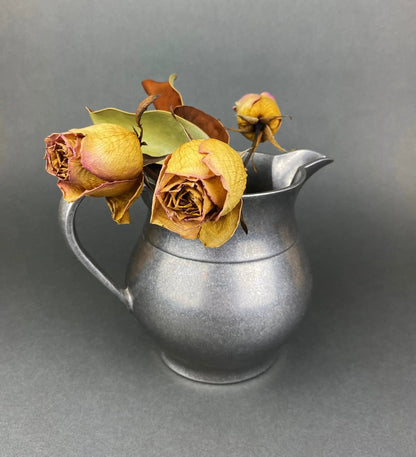 Metal pitcher vase with dried yellow roses centerpiece against gray backdrop on Tampa Home & Garden Store