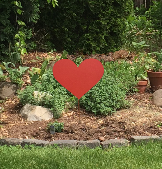 Red metal heart garden stake in a landscaped garden with mulch and rocks, Rustica Ornamentals on Tampa Home & Garden Store