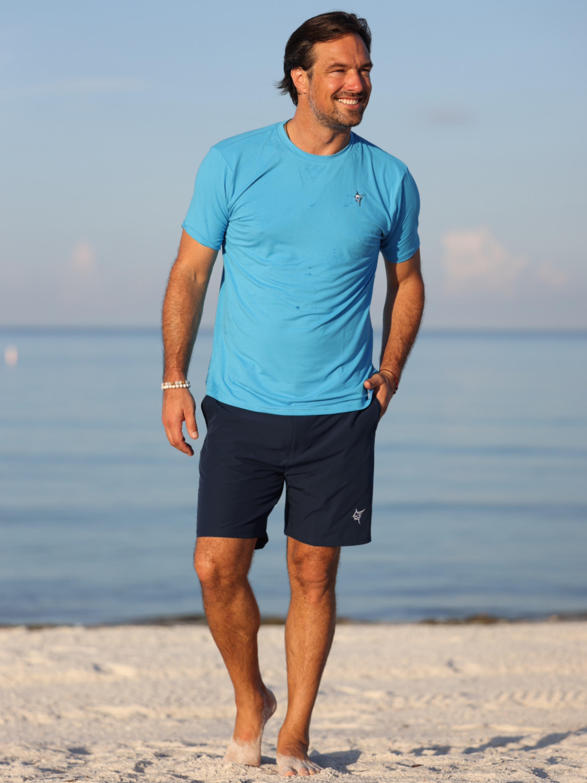 Grander Short Sleeve Performance Tee by White Water Life in light blue worn by a man at the beach on Tampa Home & Garden Store