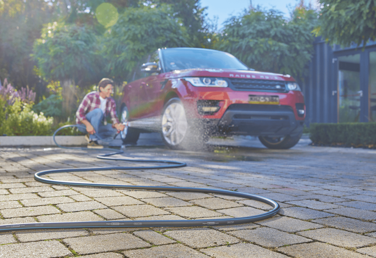 Gardena garden hose 30m 100ft 5/8 X-Flow black hose laid across driveway while a man washes a red SUV on Tampa Home & Garden Store