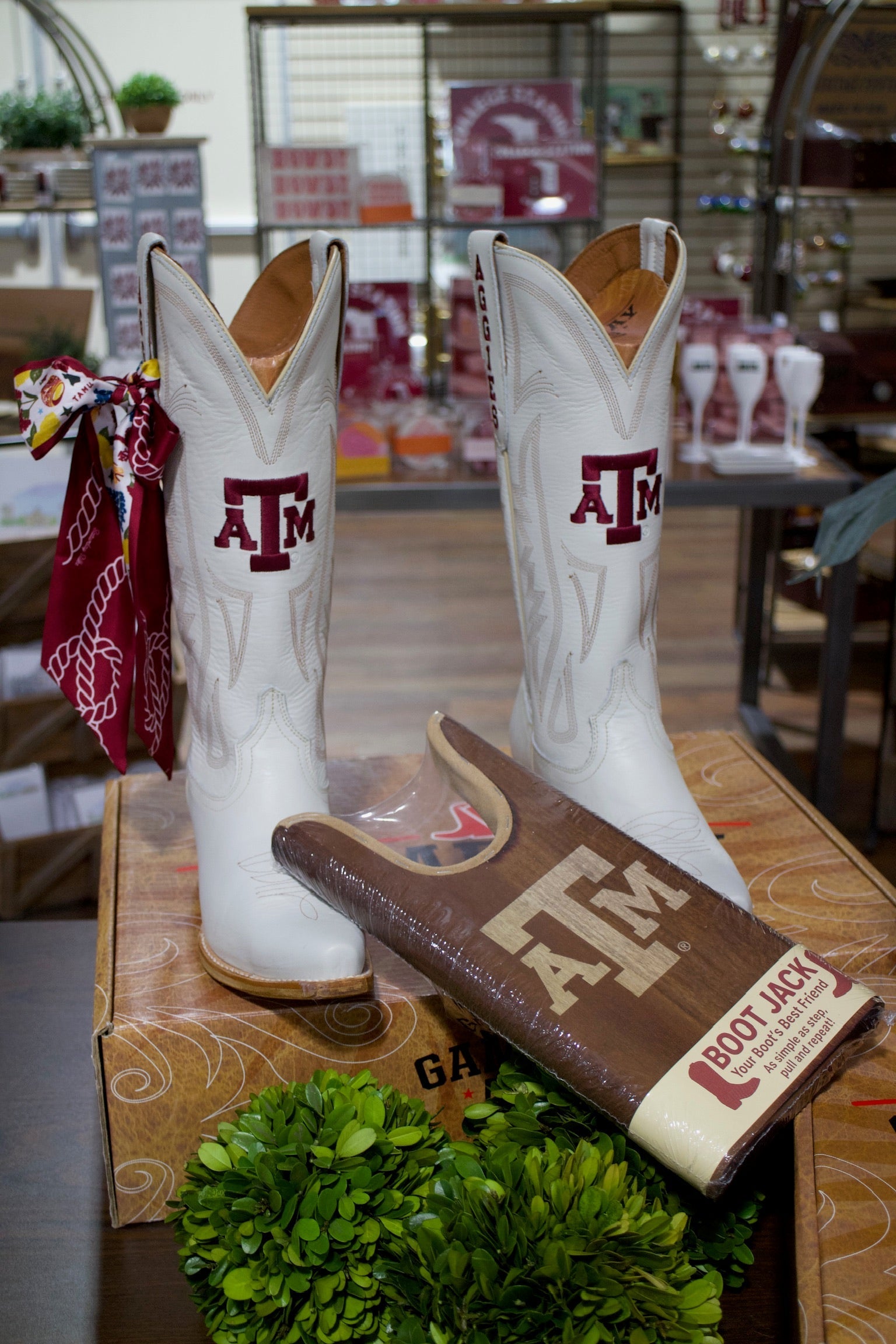 Pair of Texas A&M white cowboy boots with maroon A&M logo, red bandana on left boot on Tampa Home & Garden Store