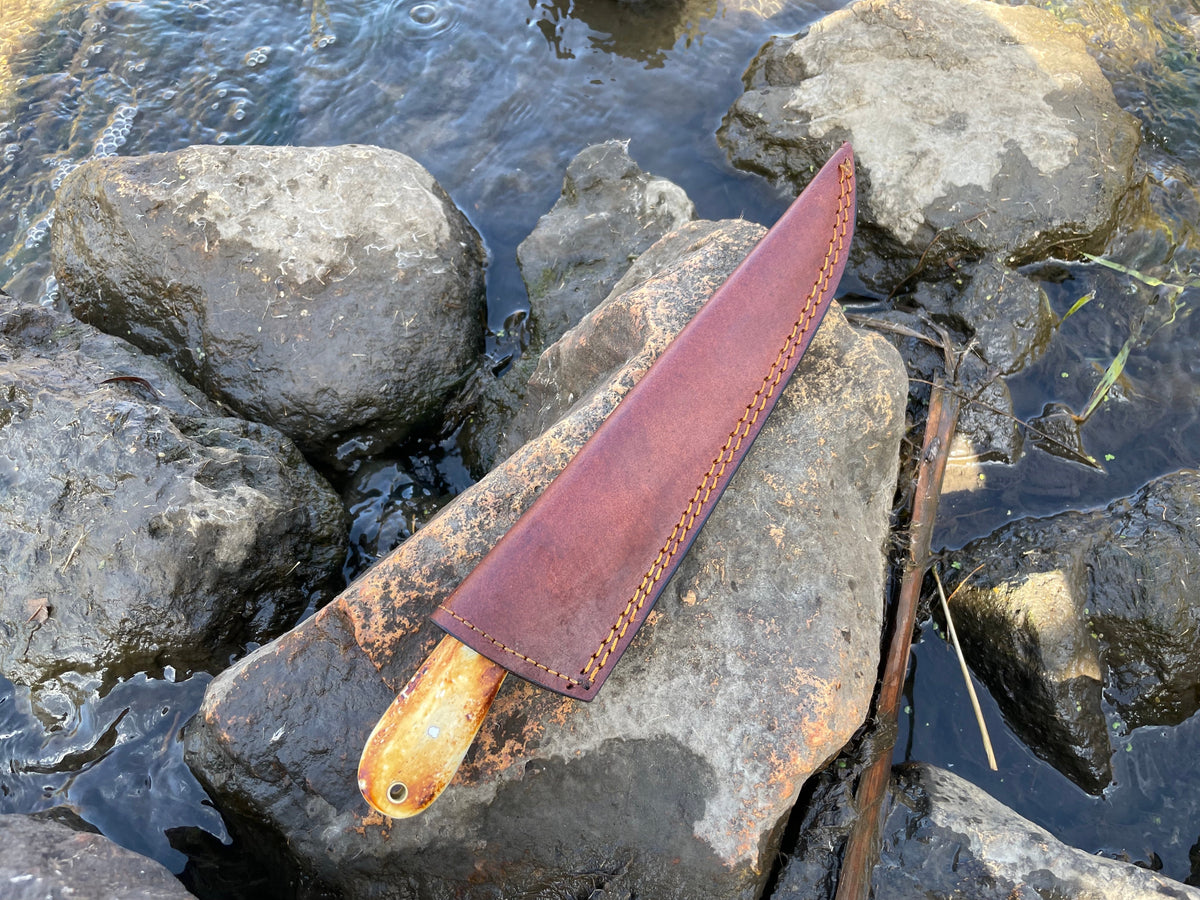 Bonning and flaying knife in brown leather sheath with orange stitching, handle on rocks by water on Tampa Home & Garden Store