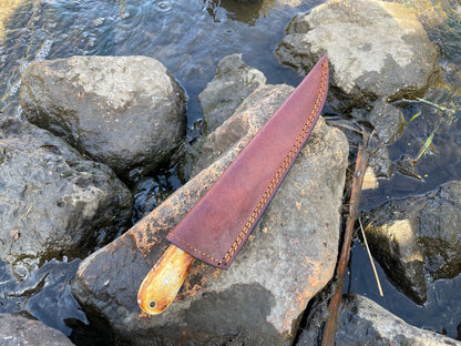 Bonning and flaying knife in brown leather sheath with orange stitching, handle on rocks by water on Tampa Home & Garden Store