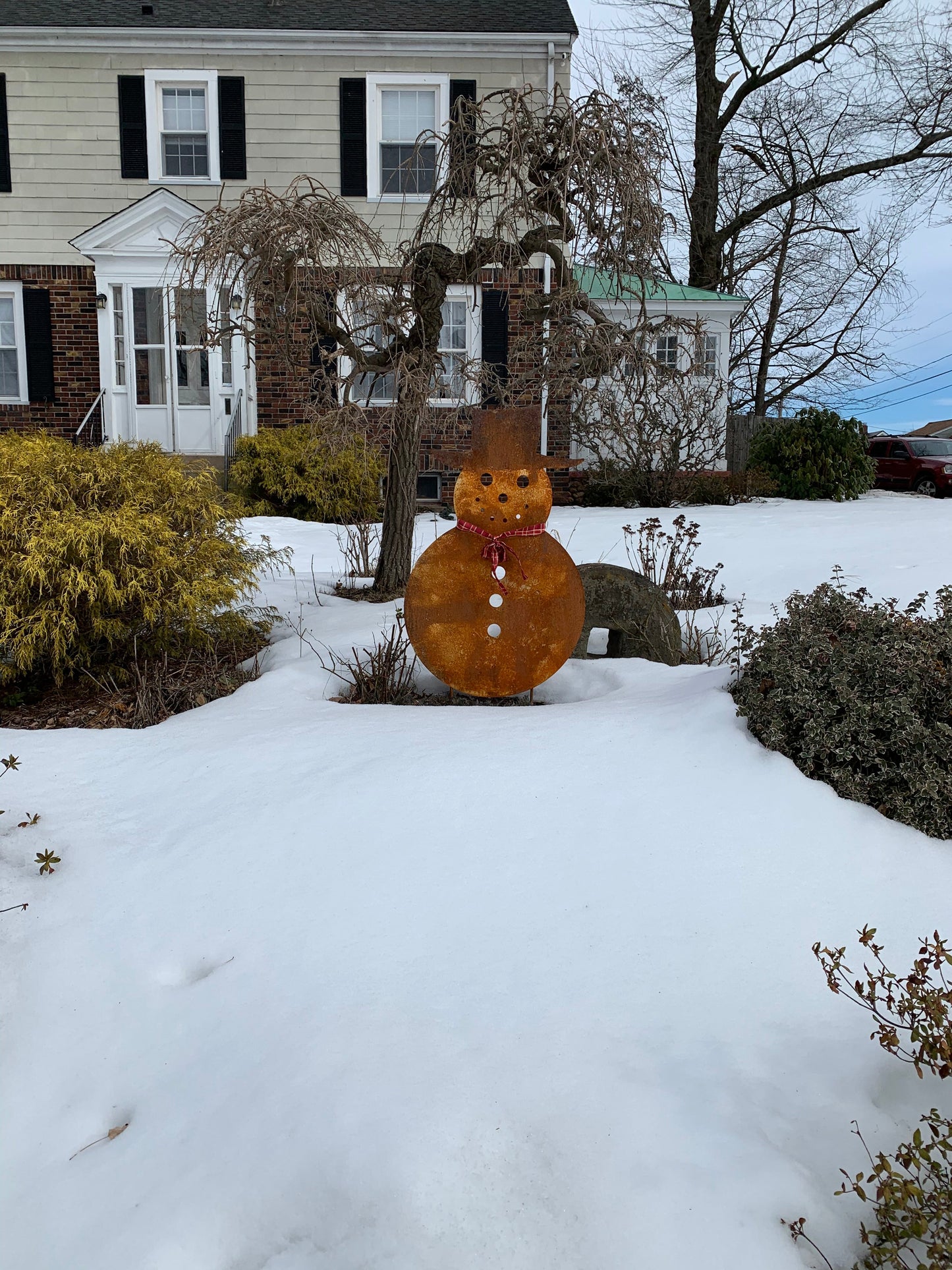 Large rust-orange outdoor snowman sculpture with top hat and red scarf in snowy front yard on Tampa Home & Garden Store