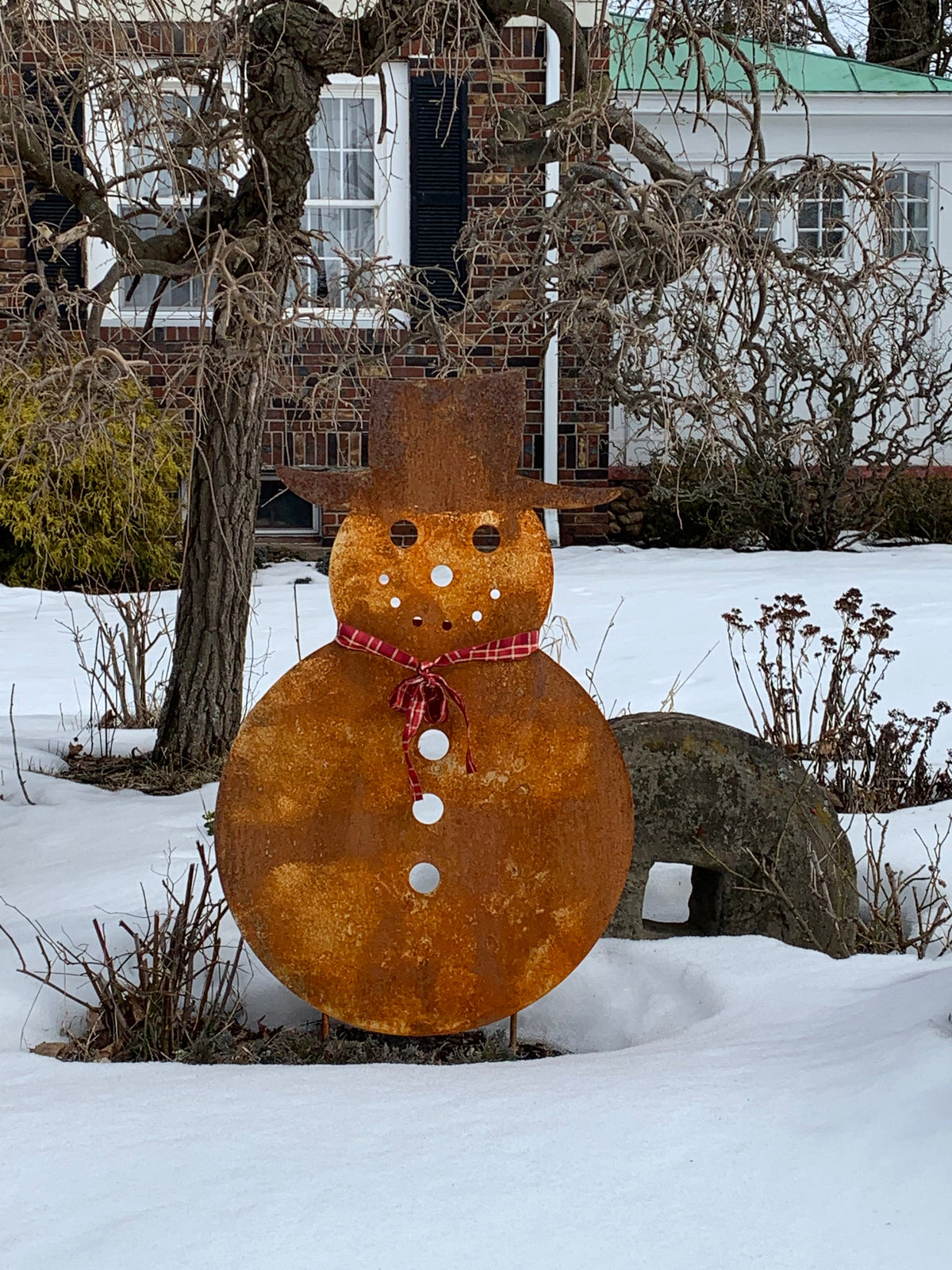 Large outdoor snowman sculpture in a rust finish with red plaid scarf in snowy yard on Tampa Home & Garden Store
