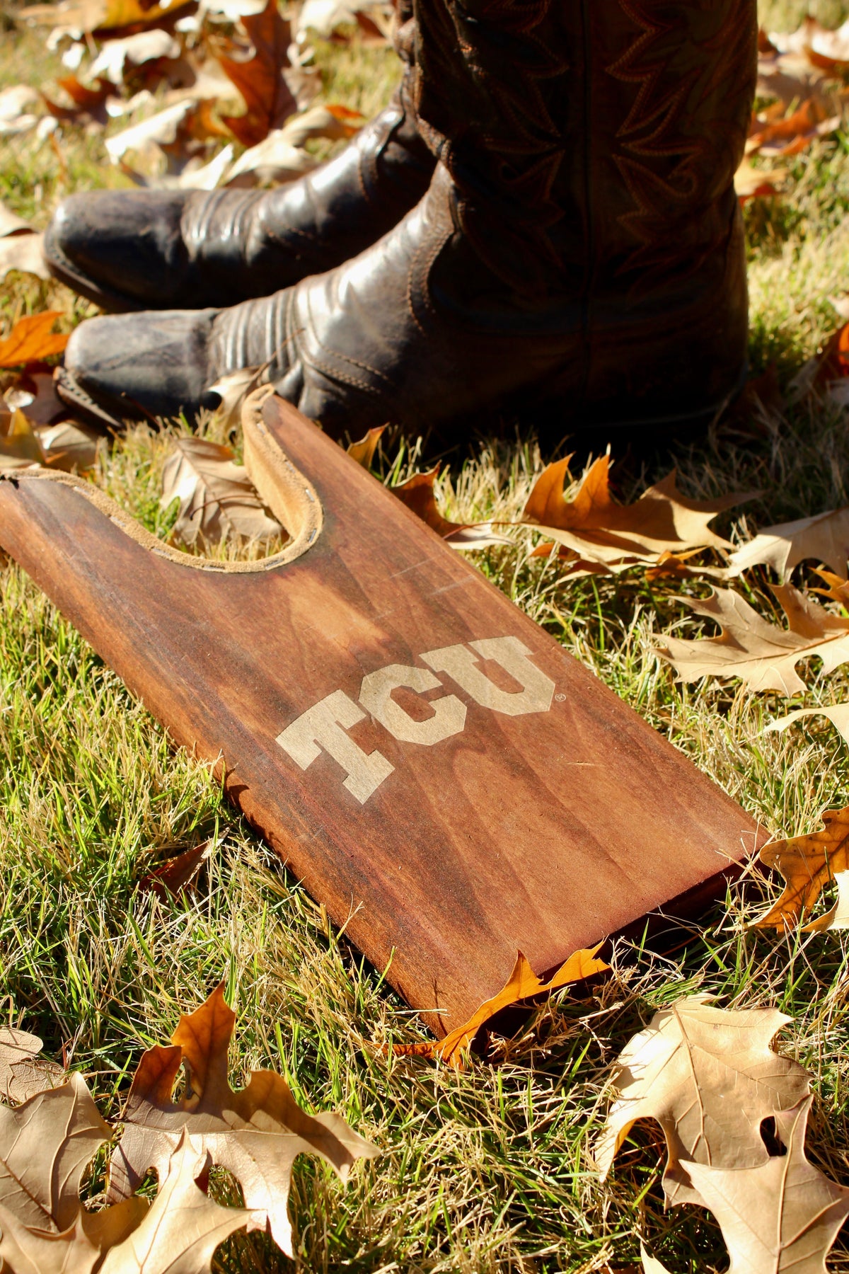 TCU boot jack by Ryan's Woodworking, pair of black leather boots on grass beside a board on Tampa Home & Garden Store
