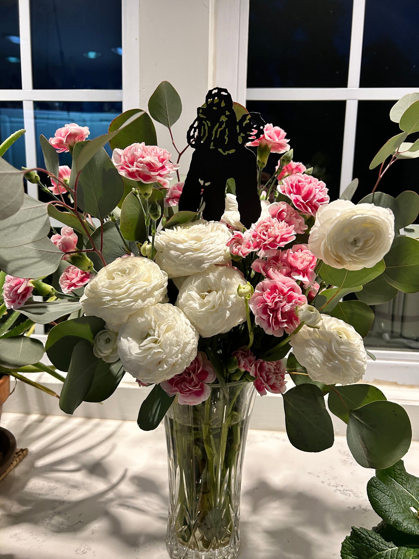 Black metal poodle ornament among pink blooms and white ranunculus in a glass vase on Tampa Home & Garden Store